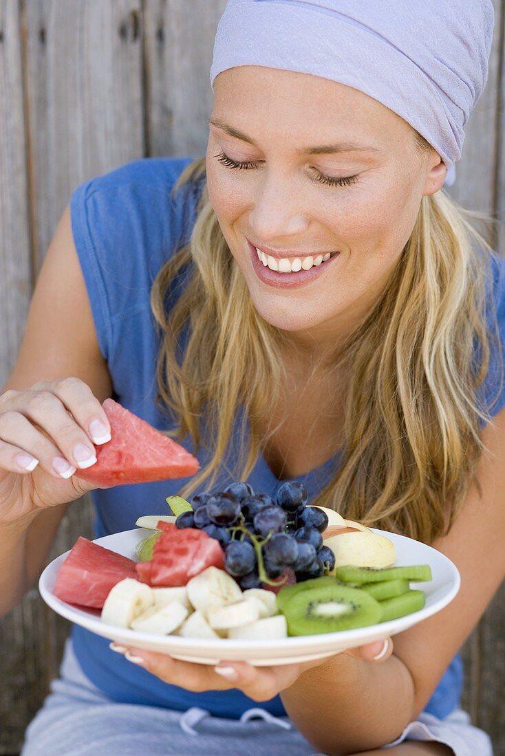 Woman eating watermelon from a plate of fruit