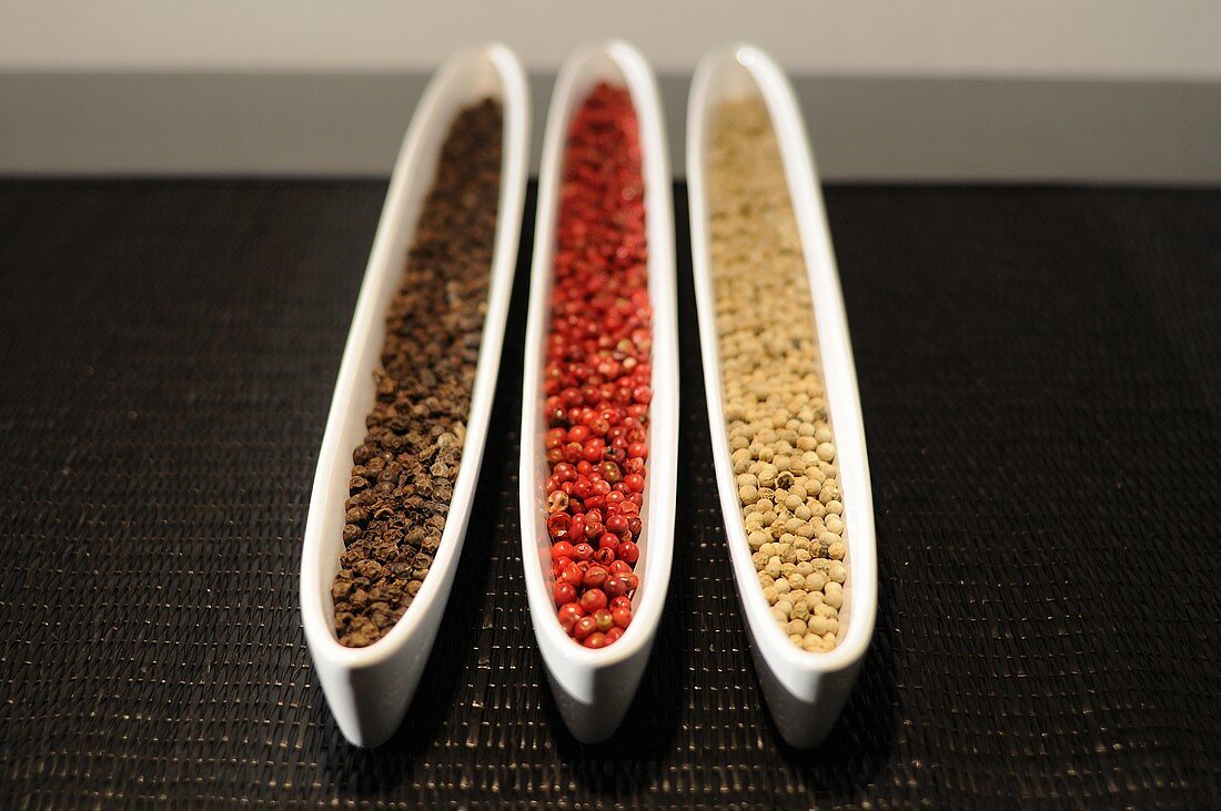 Black, red and white peppercorns in three dishes