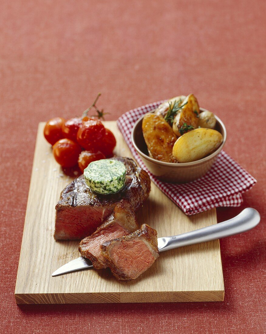 Beef steak with herb butter, roast potatoes, tomatoes