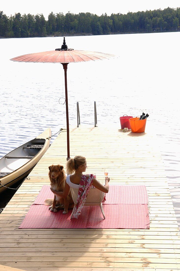 Woman with glass of strawberry Prosecco & dog on landing stage