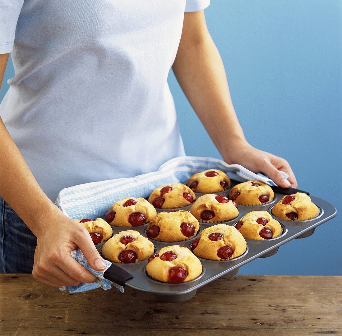 Frau hält ein Backblech mit Kirschmuffins