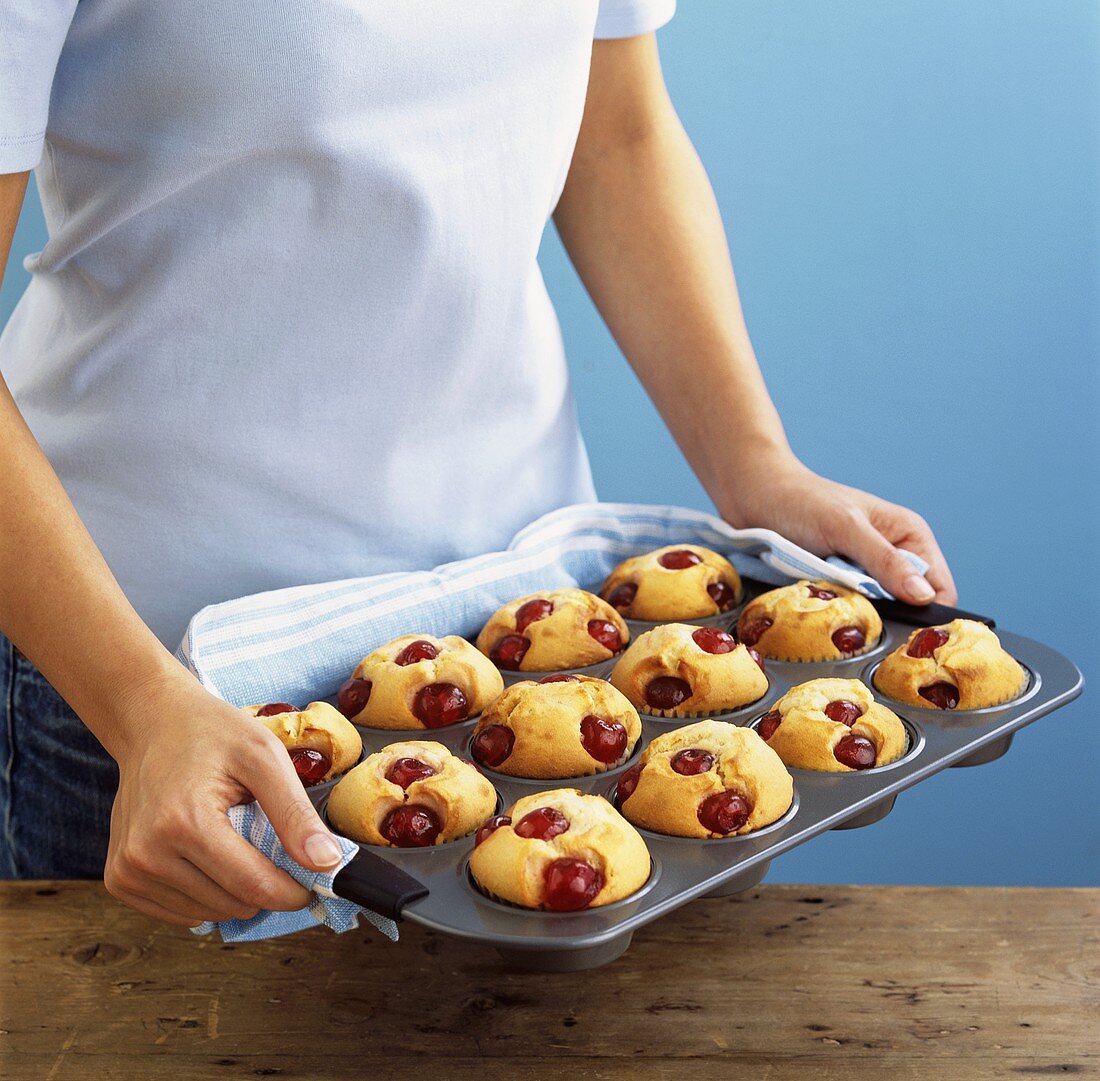 Woman holding a tray of cherry muffins