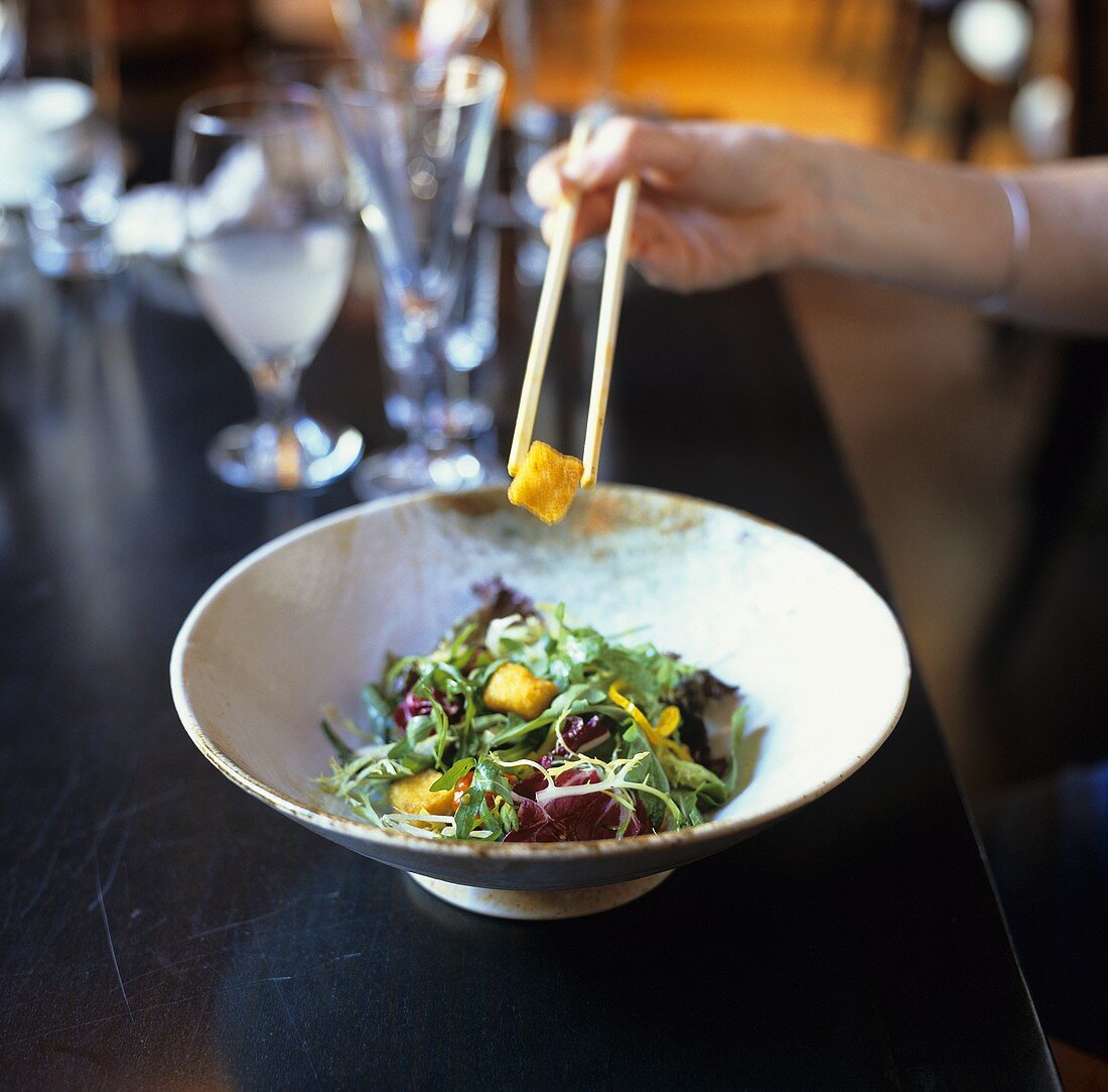 Mixed salad leaves with croutons being eaten with chopsticks