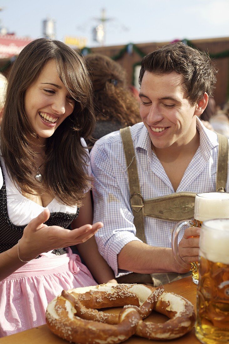 Young man & woman in traditional dress with pretzel, beer at fair