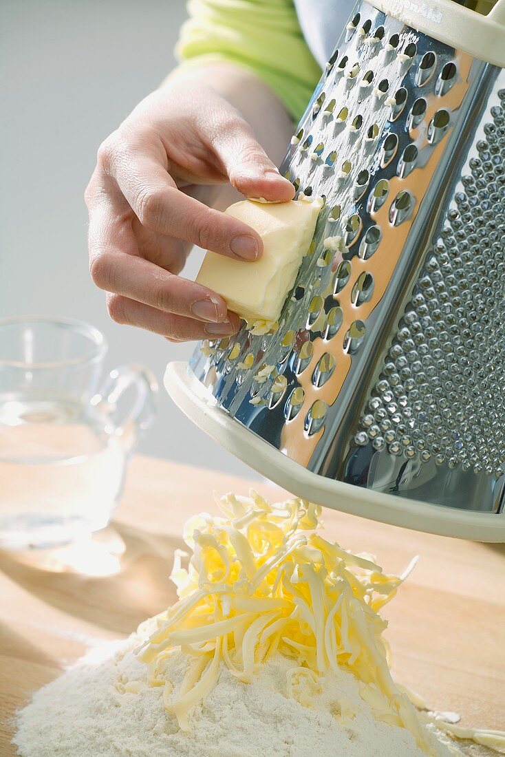 Mürbteig zubereiten: Butter wird auf Mehlhaufen geraspelt