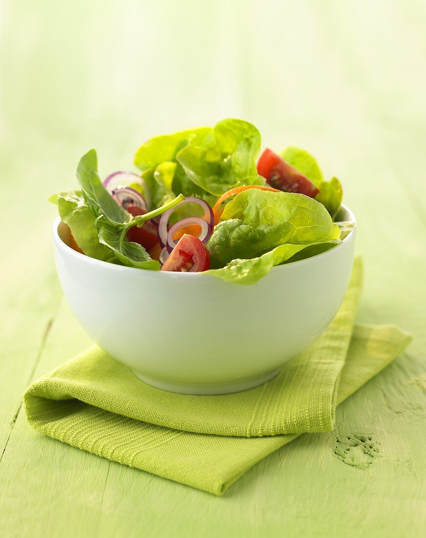 A small bowl of green salad with vegetables and basil