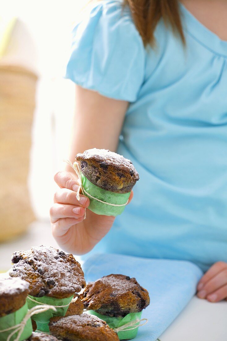 Girl holding blueberry muffin sprinkled with icing sugar