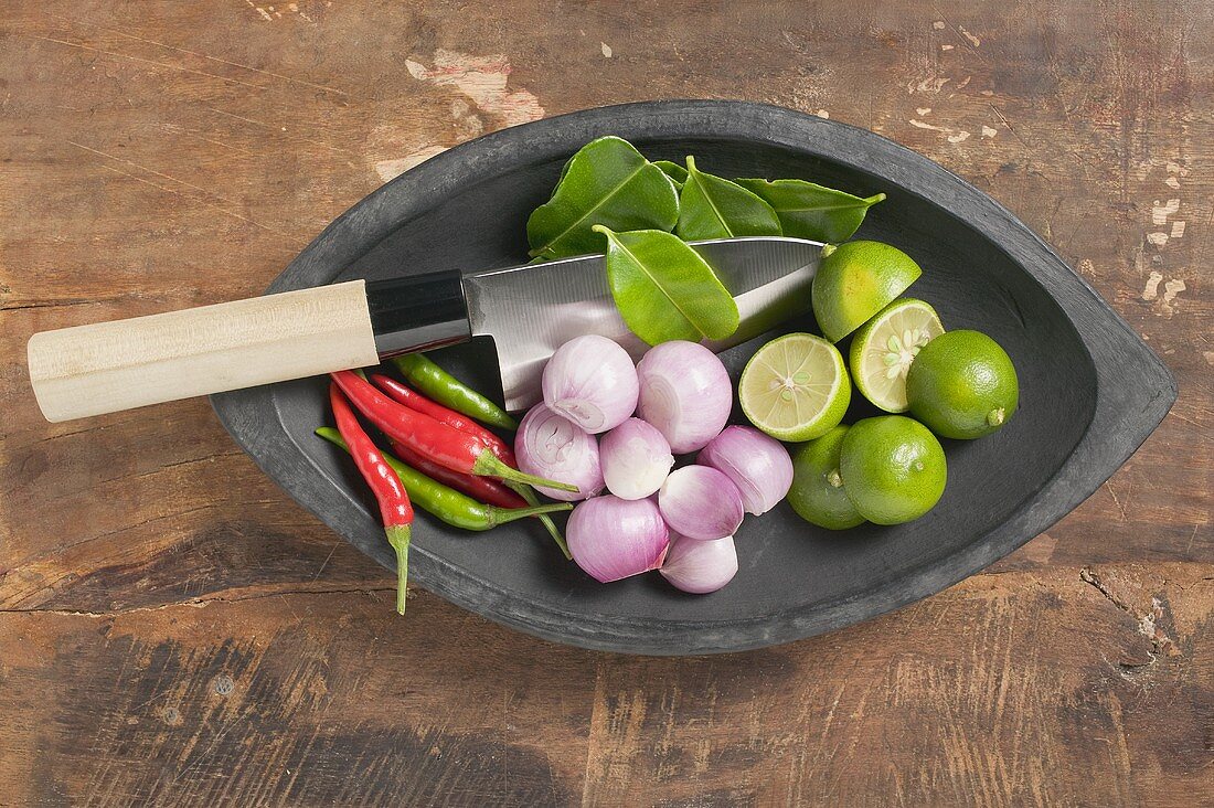A bowl of limes, lime leaves, chillis and onions
