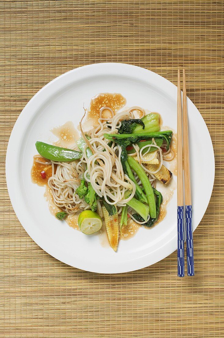 Ein asiatisches Nudelgericht mit Gemüse und ein Paar Essstäbchen