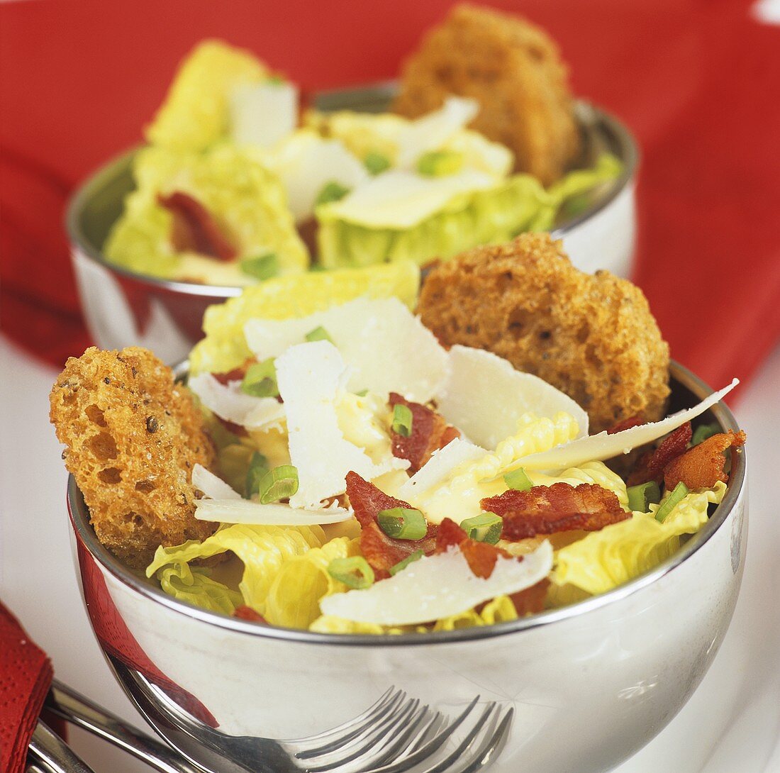 Two bowls of lettuce with fried bacon and Parmesan