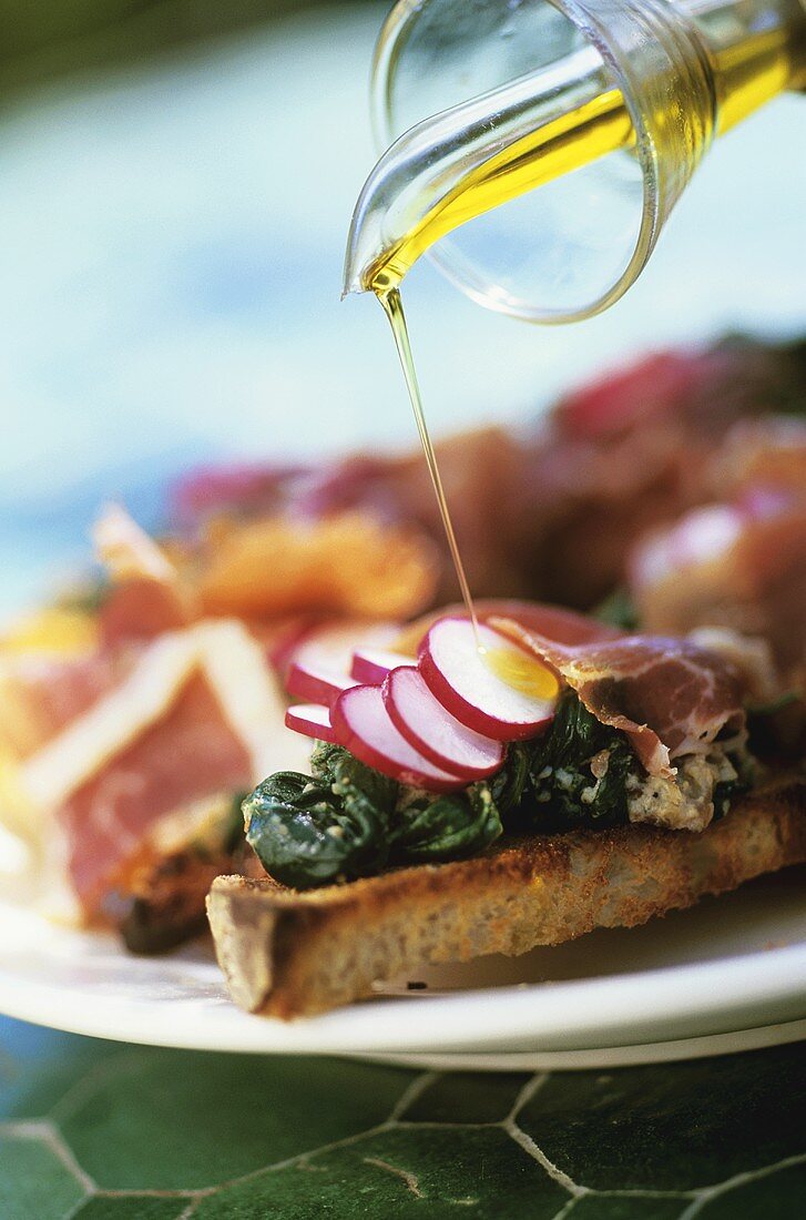 Olivenöl über geröstete Brot mit Spinat und Schinken gießen