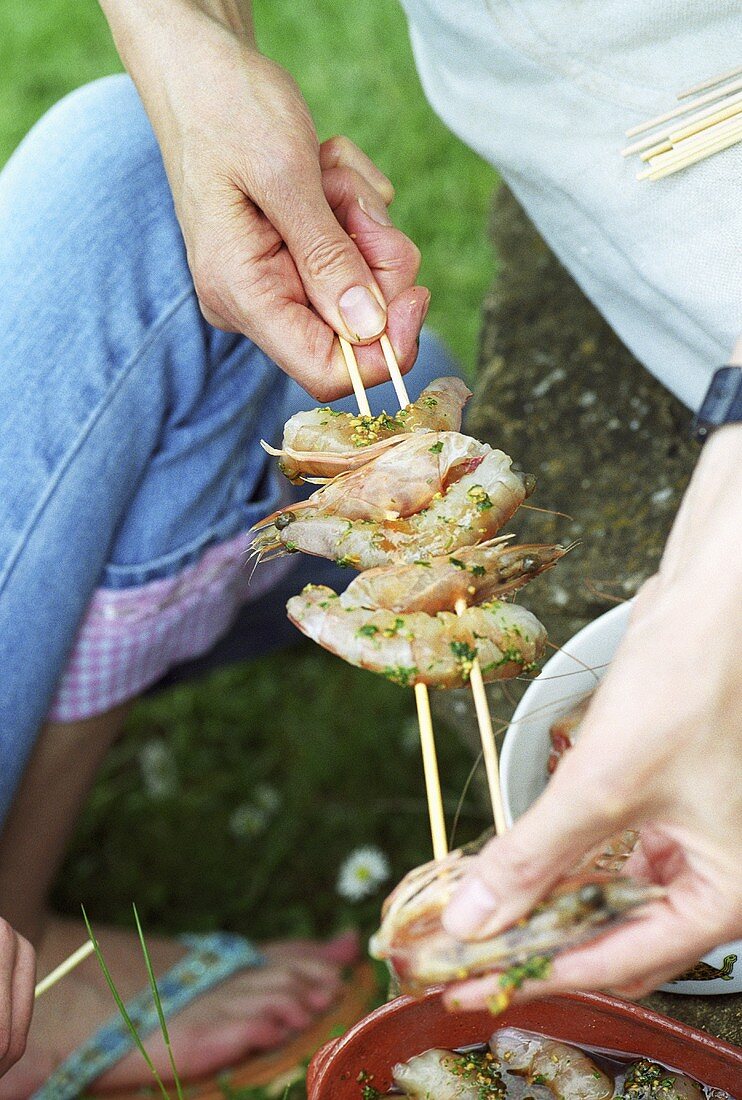 Putting marinated prawns on skewers ready for grilling