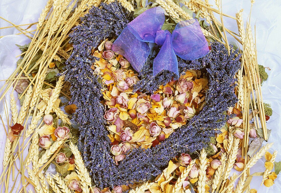 Herz aus getrocknetem Lavendel auf Getreide und Rosenblüten