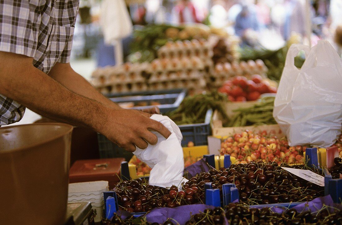 Verkäufer an einem Marktstand packt Kirschen in eine Tüte