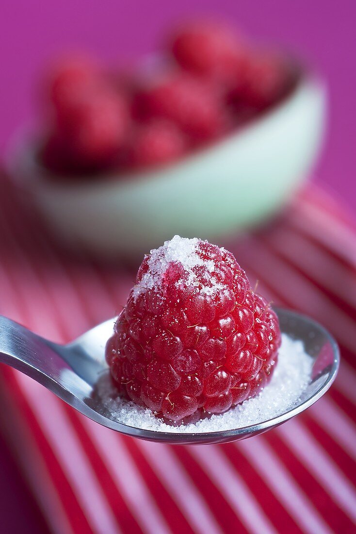 A raspberry on a spoon with sugar