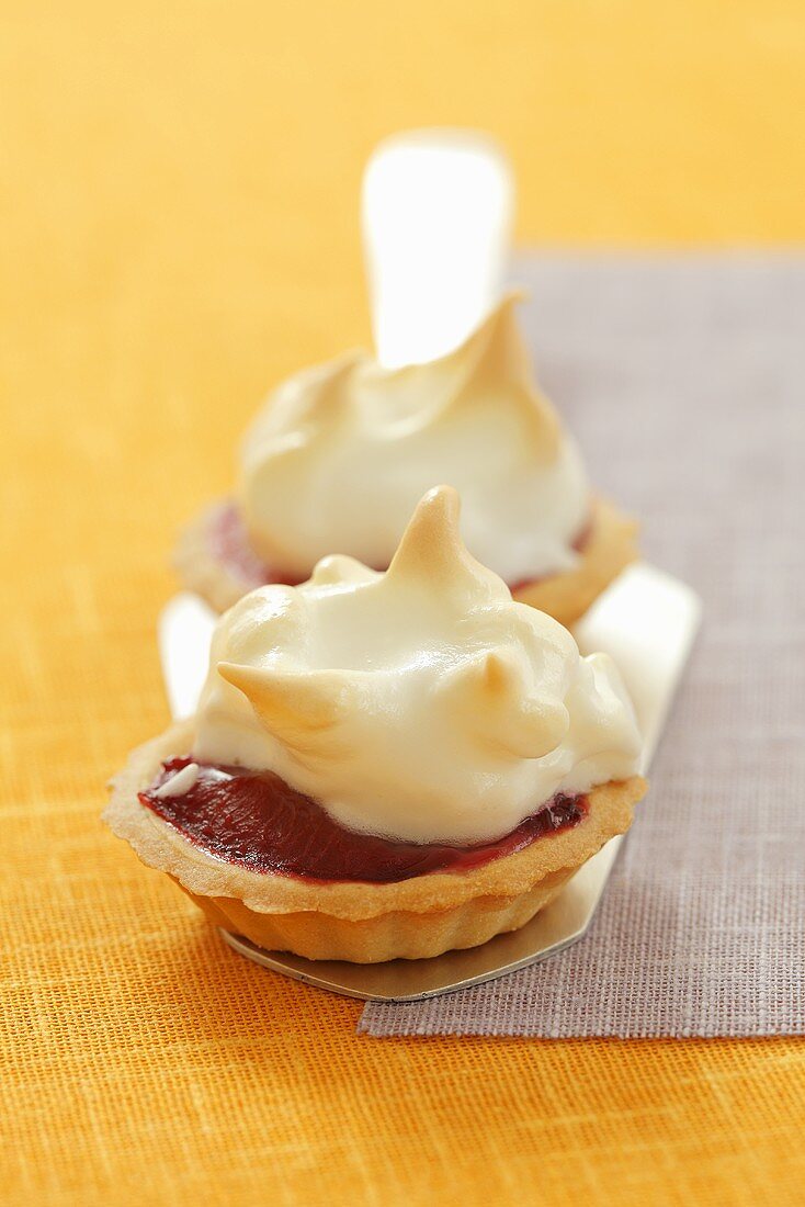 Two plum tartlets with meringue lids on a cake slice
