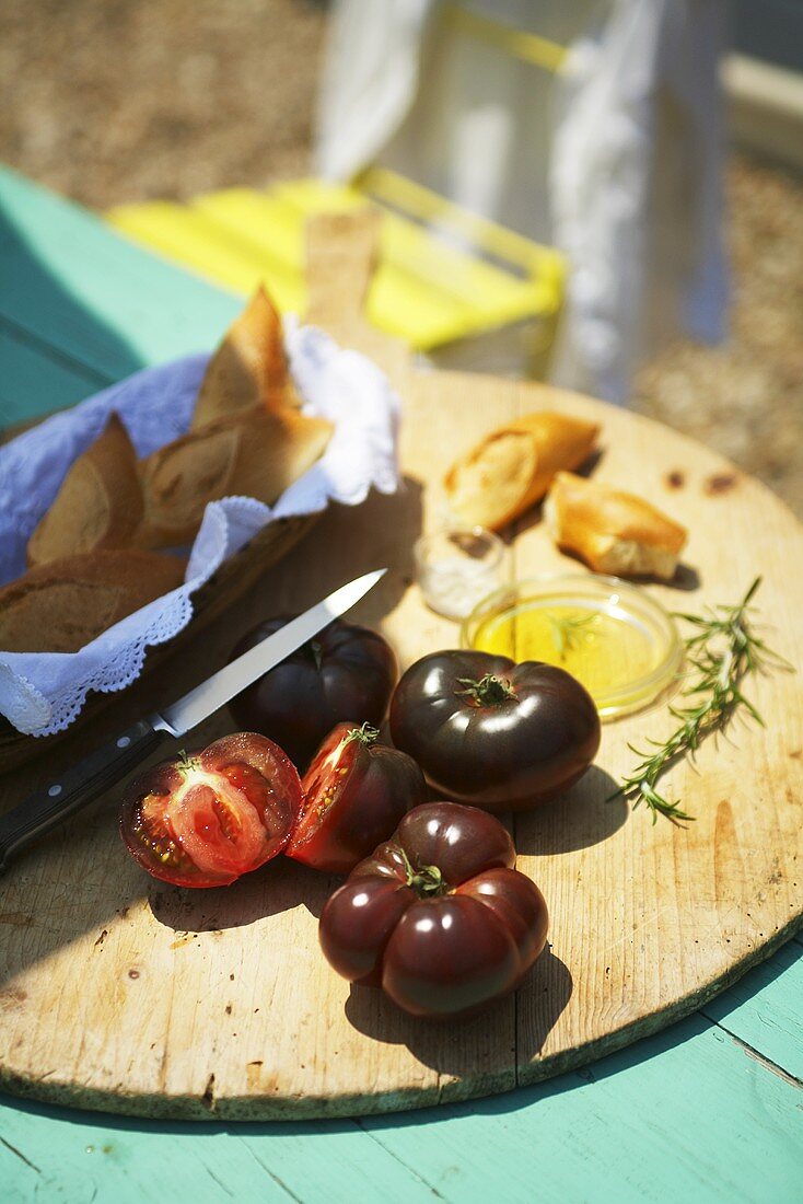 Black tomatoes, a baguette and olive oil on a garden table