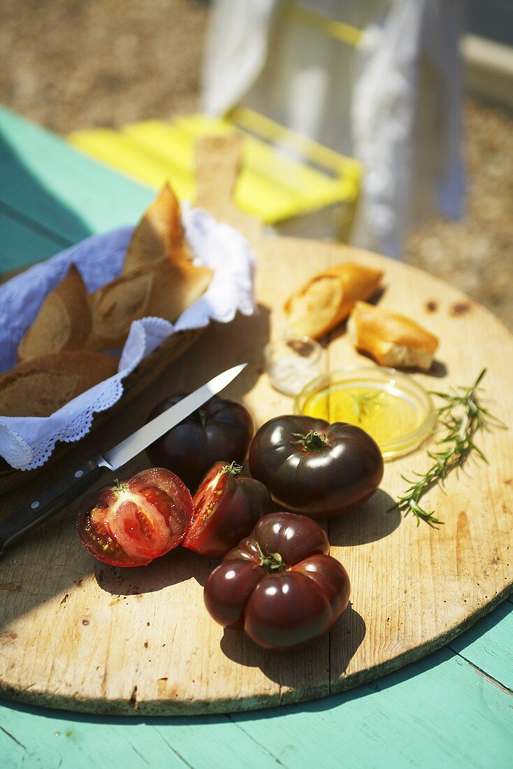 Schwarze Tomaten, Baguette und Olivenöl auf Gartentisch