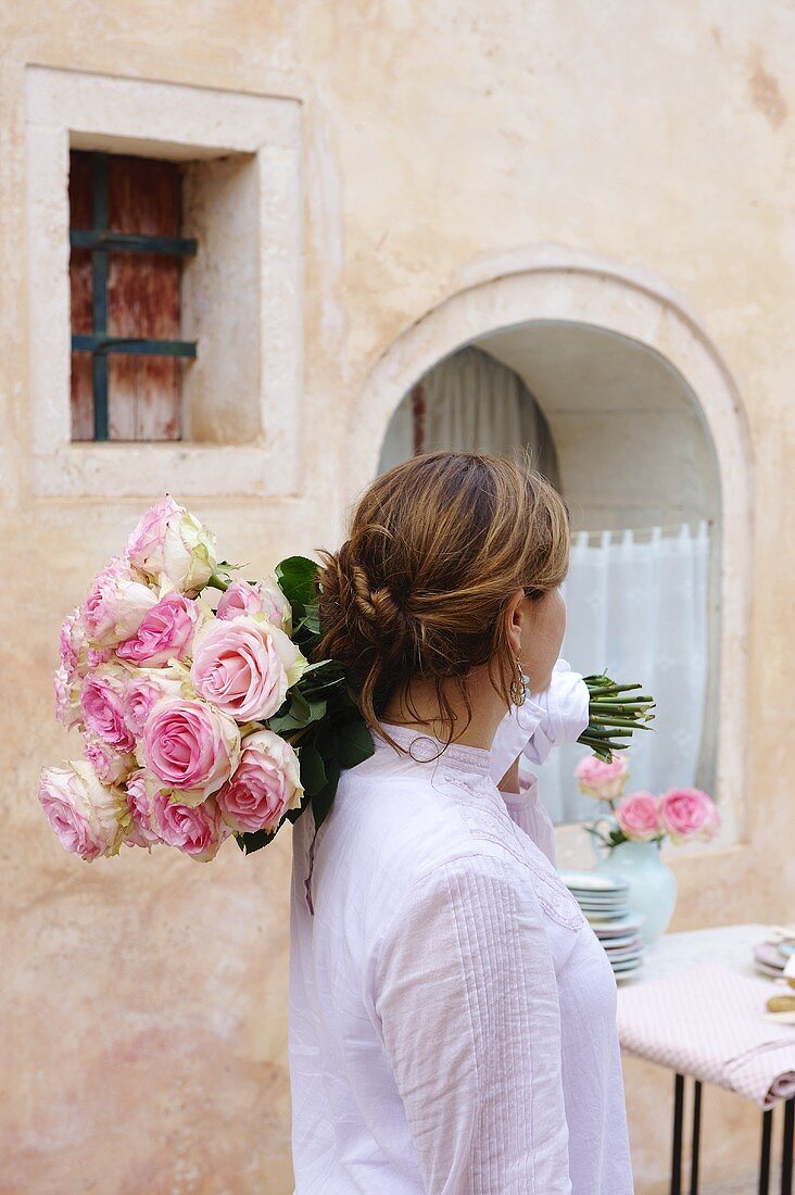 A woman carrying a bunch of roses to a garden table