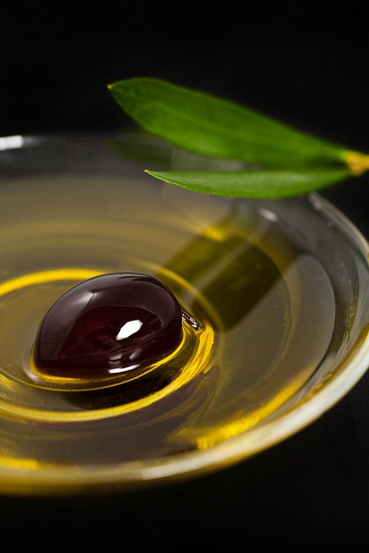 A bowl of olive oil with a black olive