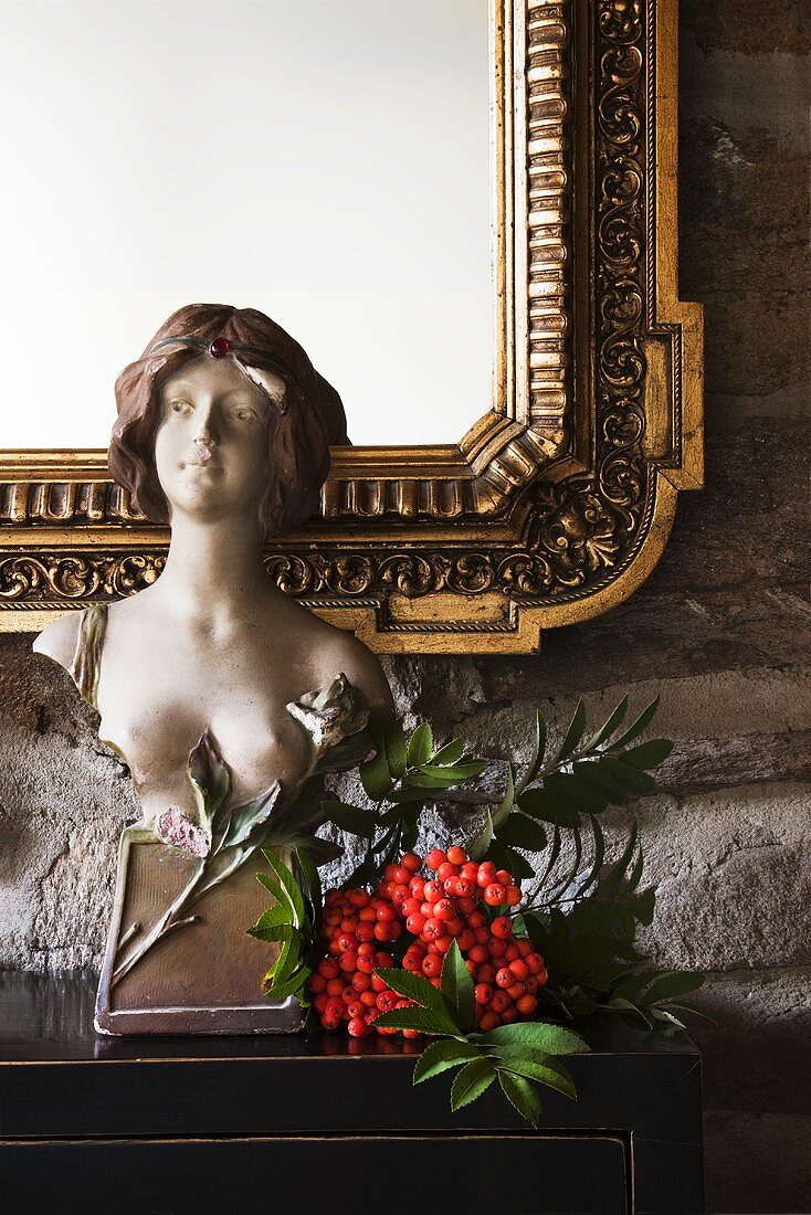 A female bust on a cupboard in front of a wall mirror