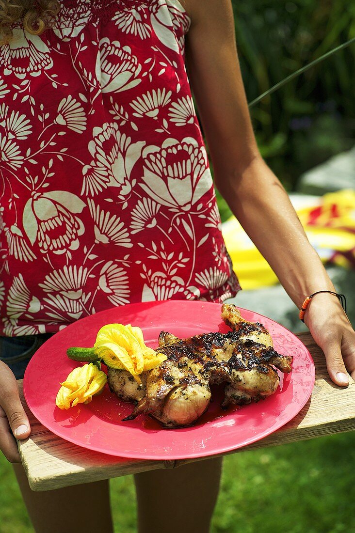 A woman serving marinated grilled chicken with courgette flowers