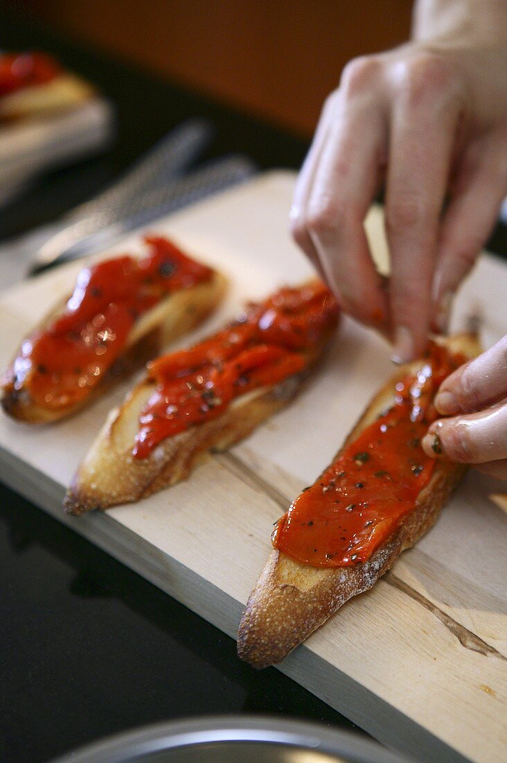 Peppers being placed on bruschetta slices