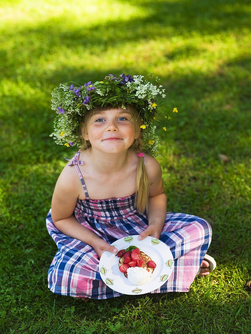 A little girl with a crown of flowers and a strawberry pancake