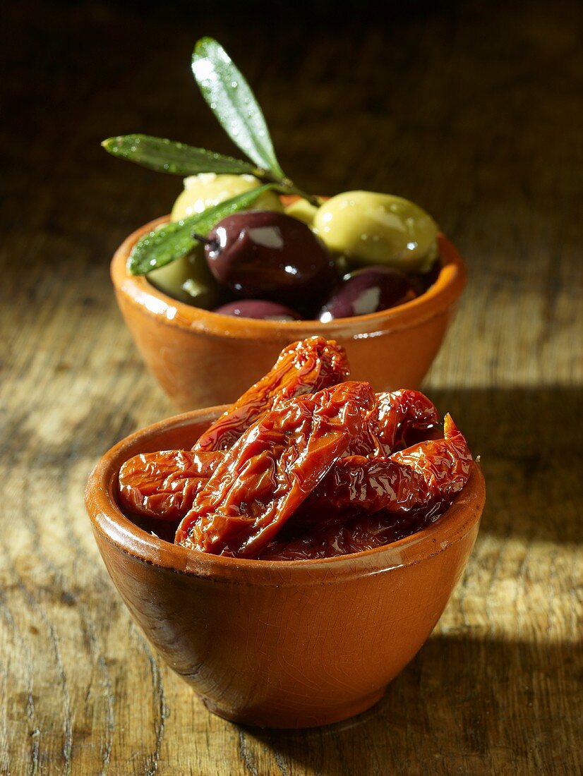 Dried tomatoes and olives in bowls on a wooden surface