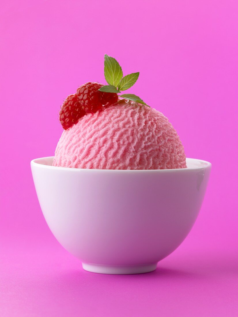 A scoop of raspberry ice cream with raspberries in white bowl