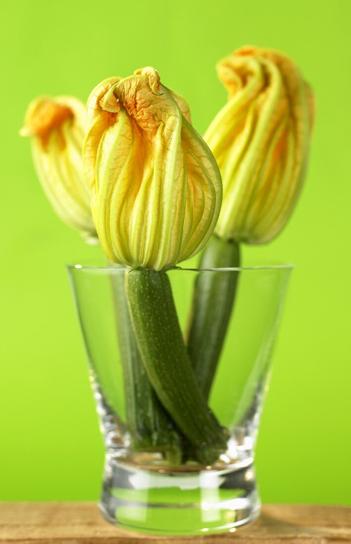 Three courgettes with flowers in a glass