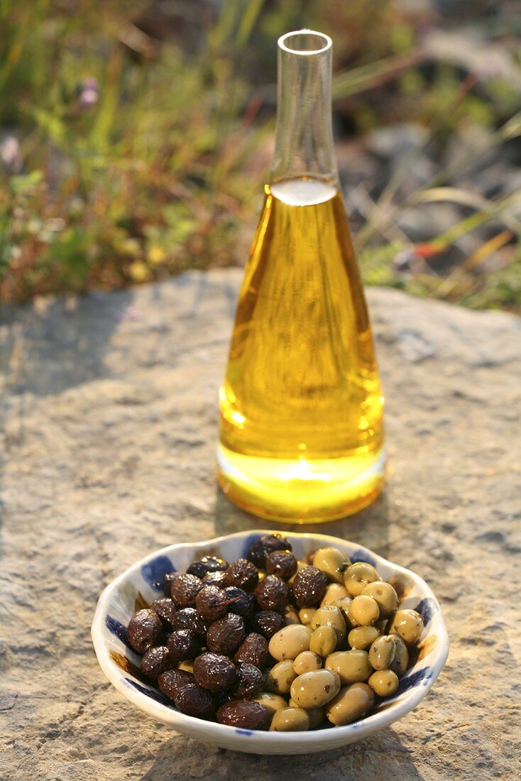 Olive oil in carafe, two types of olives in bowl out of doors