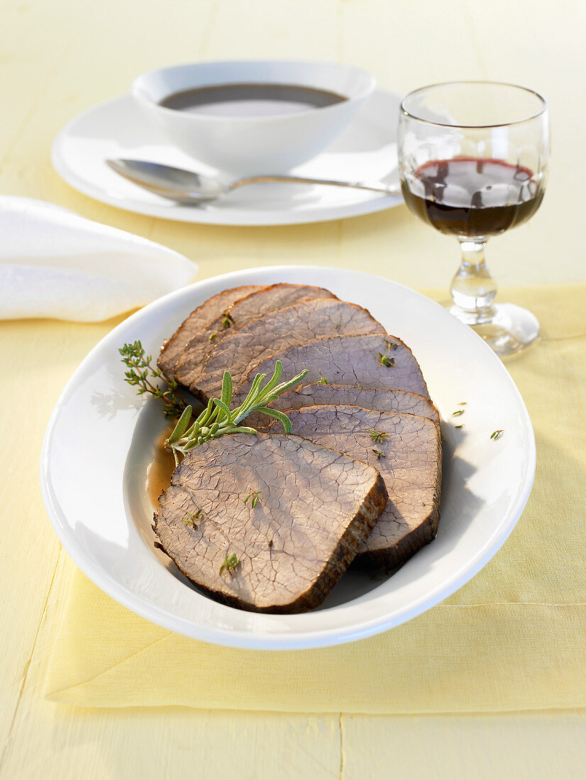 Several slices of roast beef with gravy and herbs