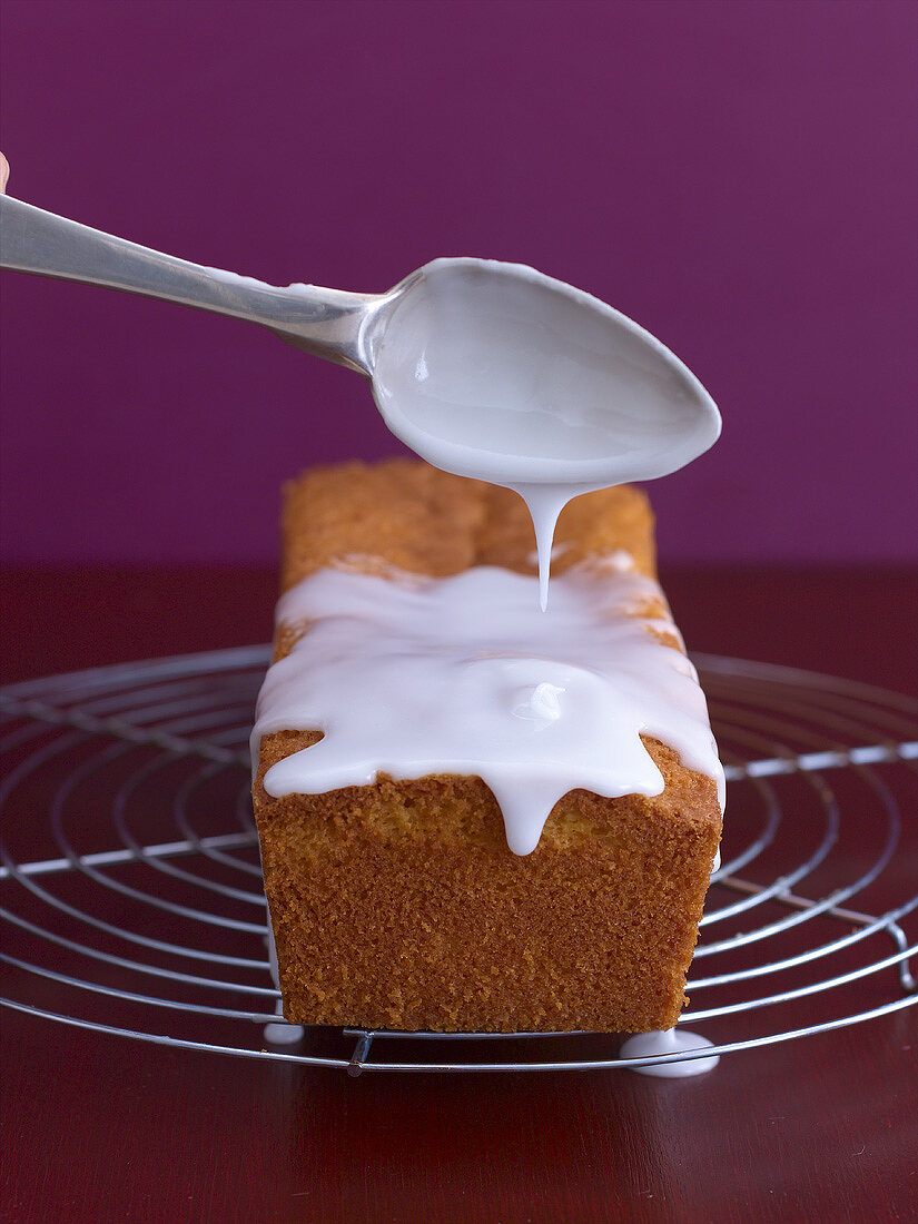 Icing being spooned over a loaf cake on a cake rack