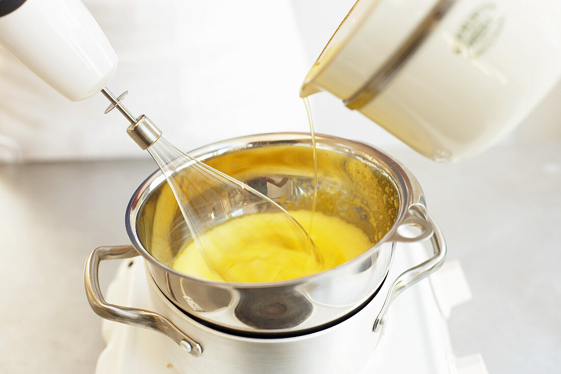 Melted butter being poured into beaten egg yolks in bain-marie