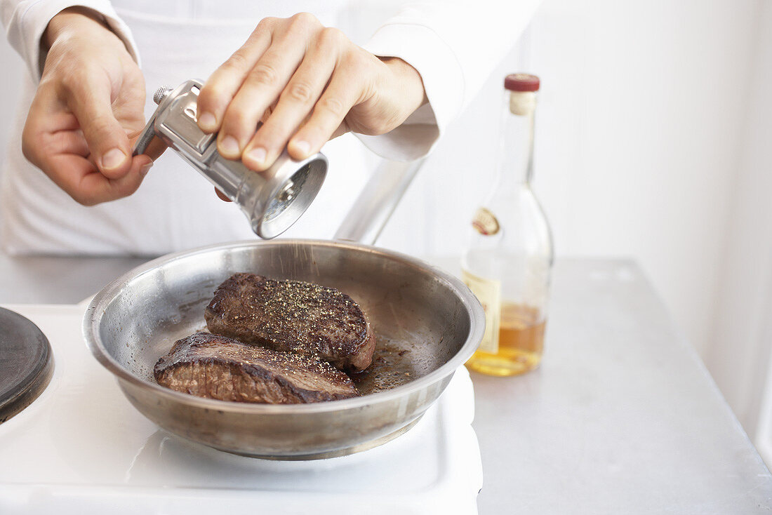 Man putting pepper on fillet steaks in a frying pan