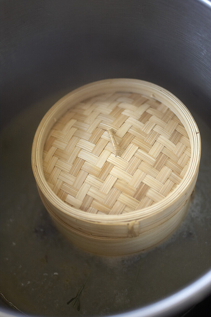 Bamboo steamer in a large pan with white wine stock