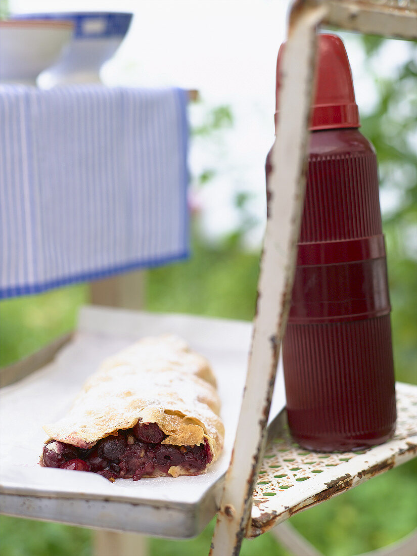 A cherry strudel with Thermos flask out of doors