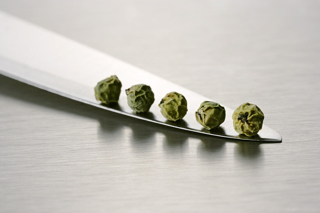 Five green peppercorns on a knife blade