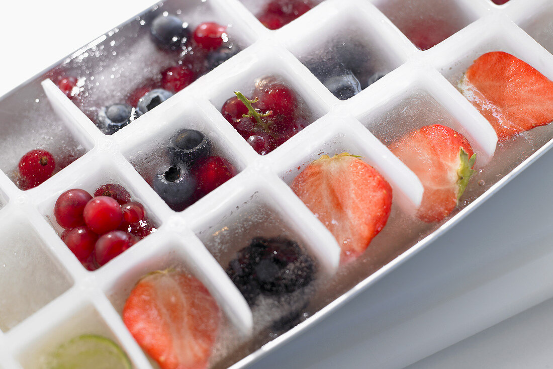 Eiswürfel mit gefrorenen Beeren in einem Eiswürfelbehälter