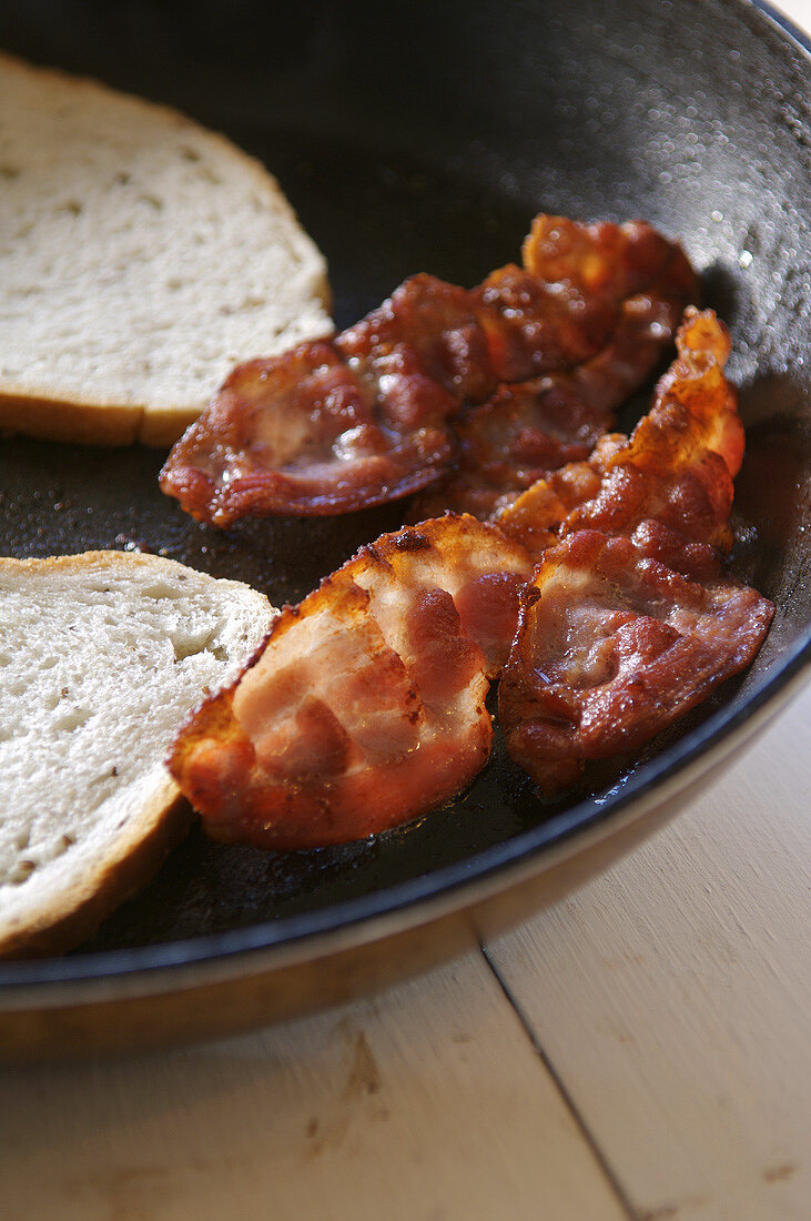 Speck- und Weissbrotscheiben braten in einer Pfanne