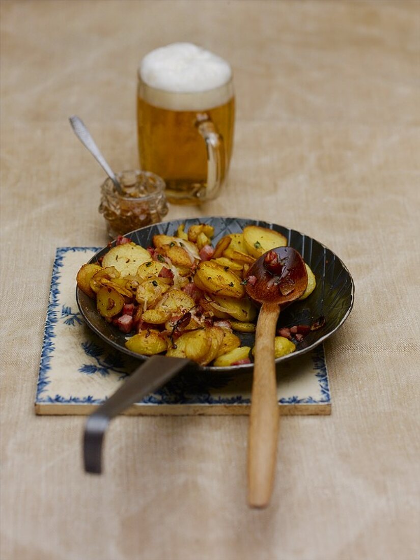 Potato and bacon hash in a frying pan and a glass of beer