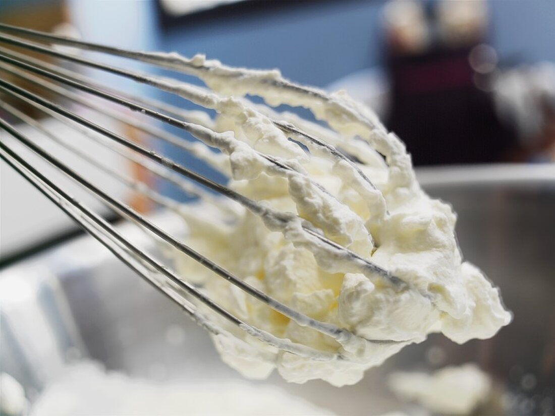 Whipped cream on a whisk with mixing bowl