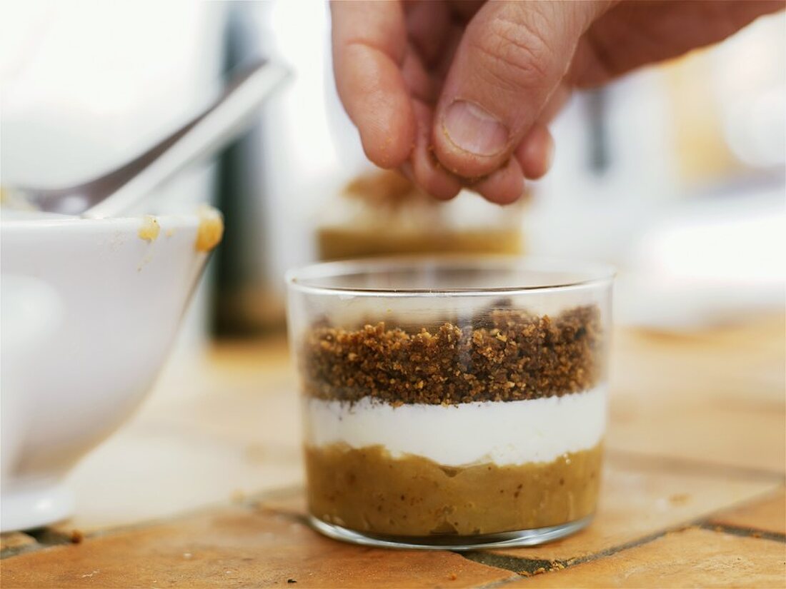 Hand sprinkling breadcrumbs on layered dessert in glass