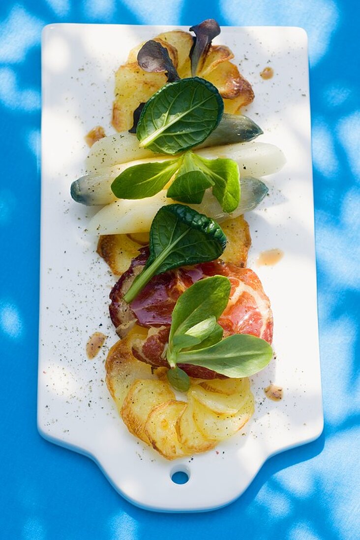 Baked potato slices with asparagus, ham and salad leaves