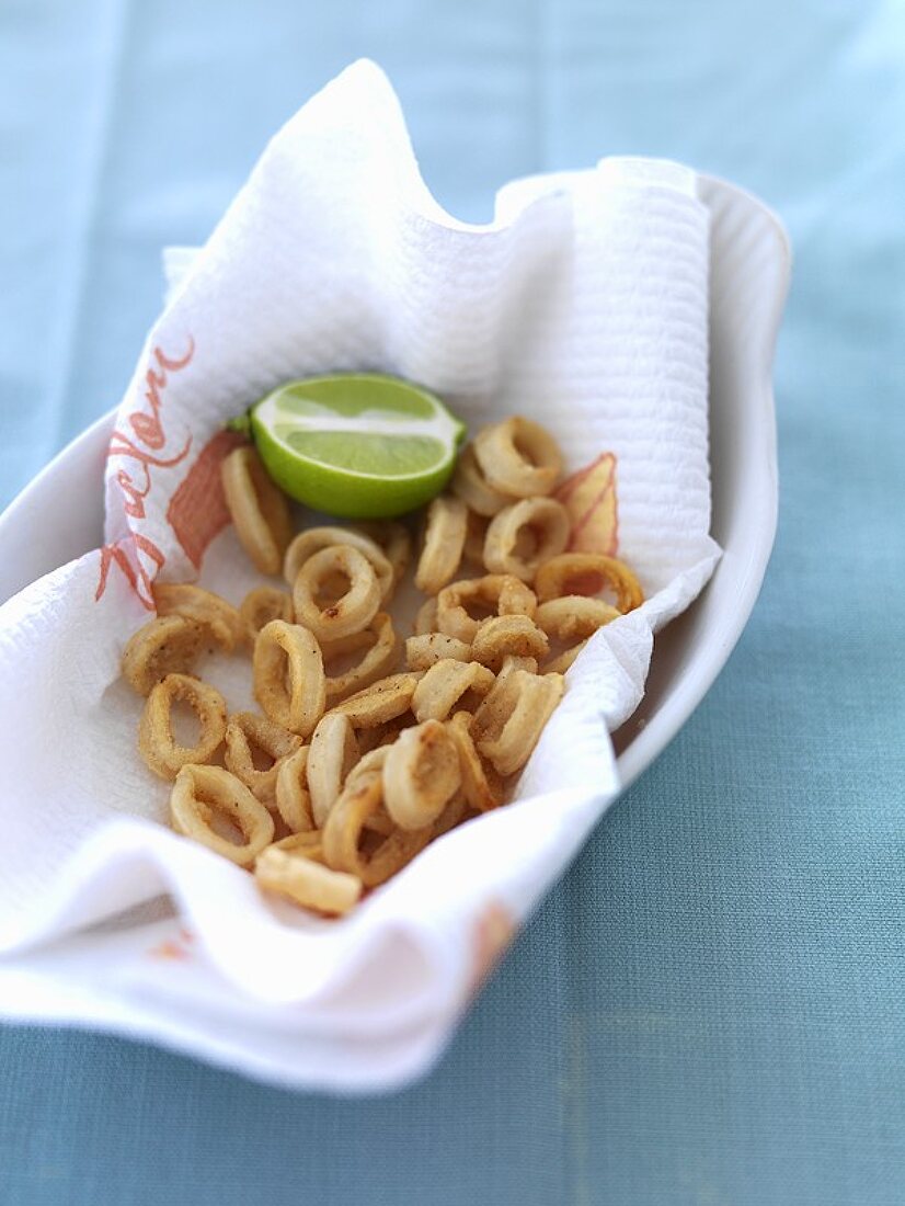 Fried calamari rings with lime on kitchen paper