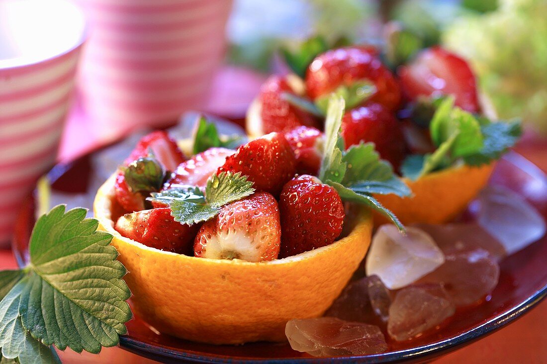 Frische Erdbeeren in Orangenschalen auf Eiswürfeln