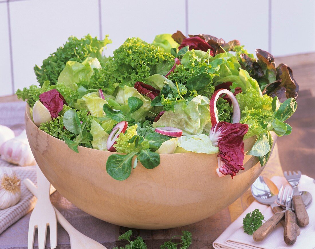 Mixed salad leaves with red onion in a wooden bowl