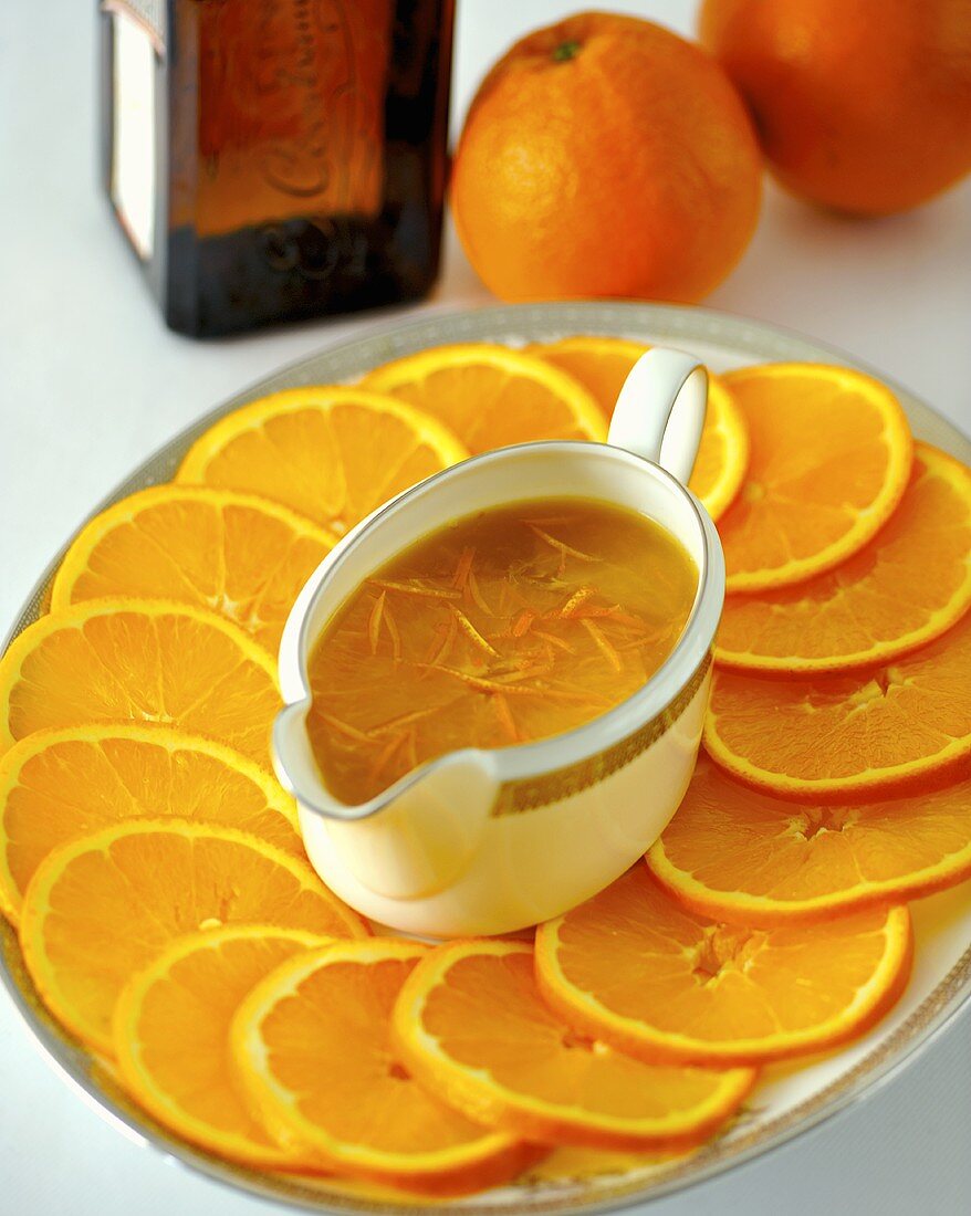 Orangensauce in Sauciere auf einer Platte mit Orangenscheiben