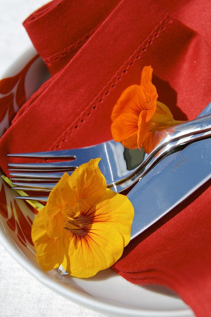 Cutlery, napkin and nasturtiums on plate